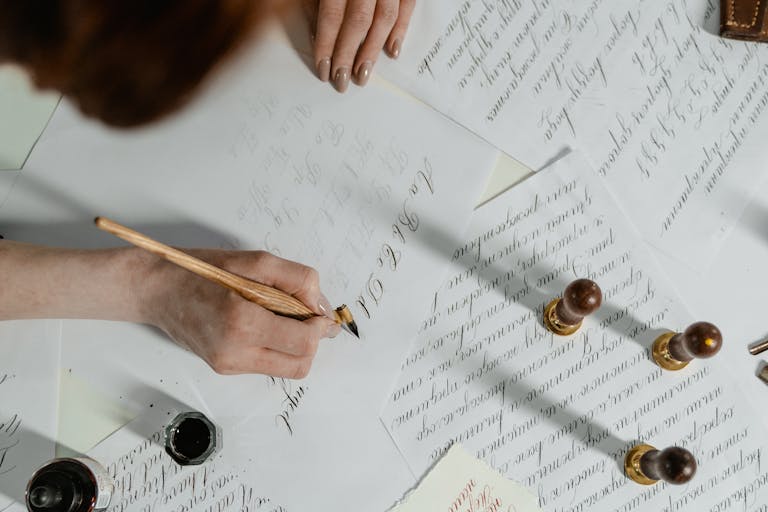 A woman's hand expertly creates calligraphy with a quill pen, showcasing elegant handwriting and calligraphy tools.