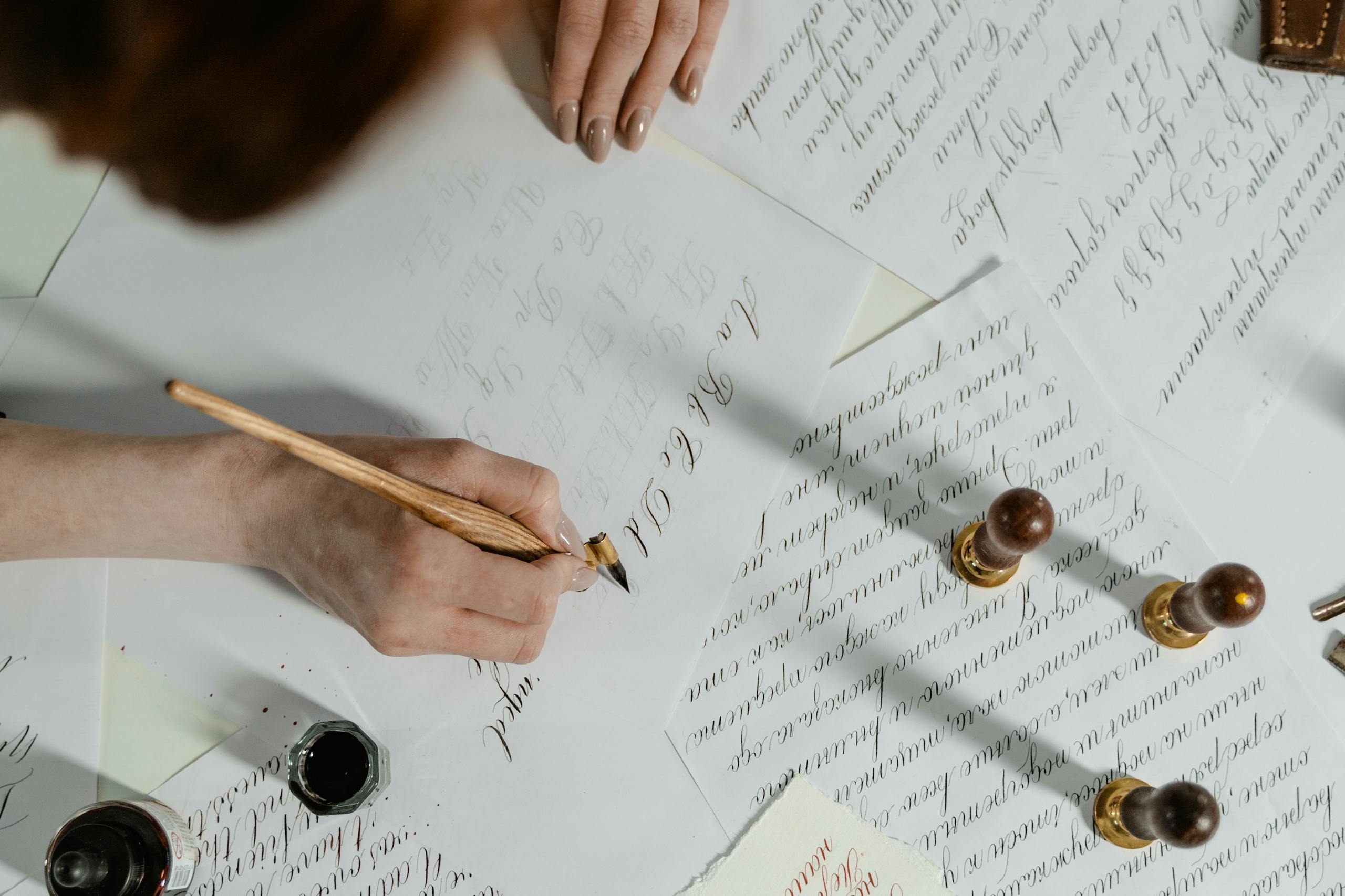 A woman's hand expertly creates calligraphy with a quill pen, showcasing elegant handwriting and calligraphy tools.