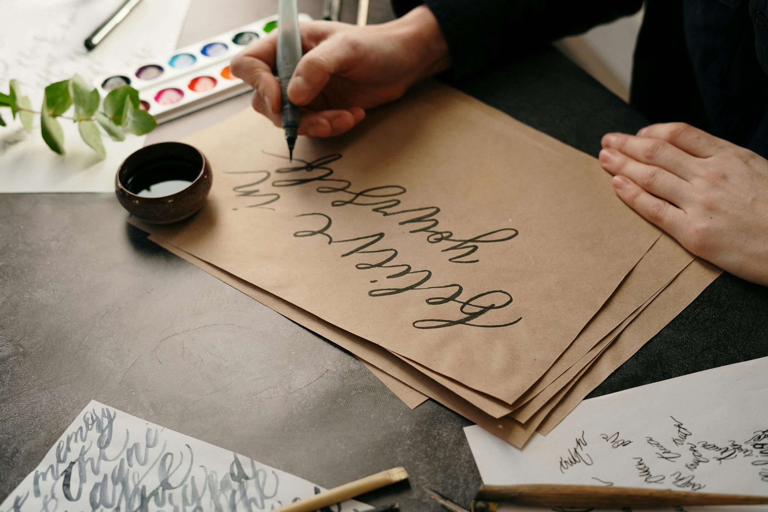 Close-up of hands creating elegant calligraphy on craft paper with artistic tools.