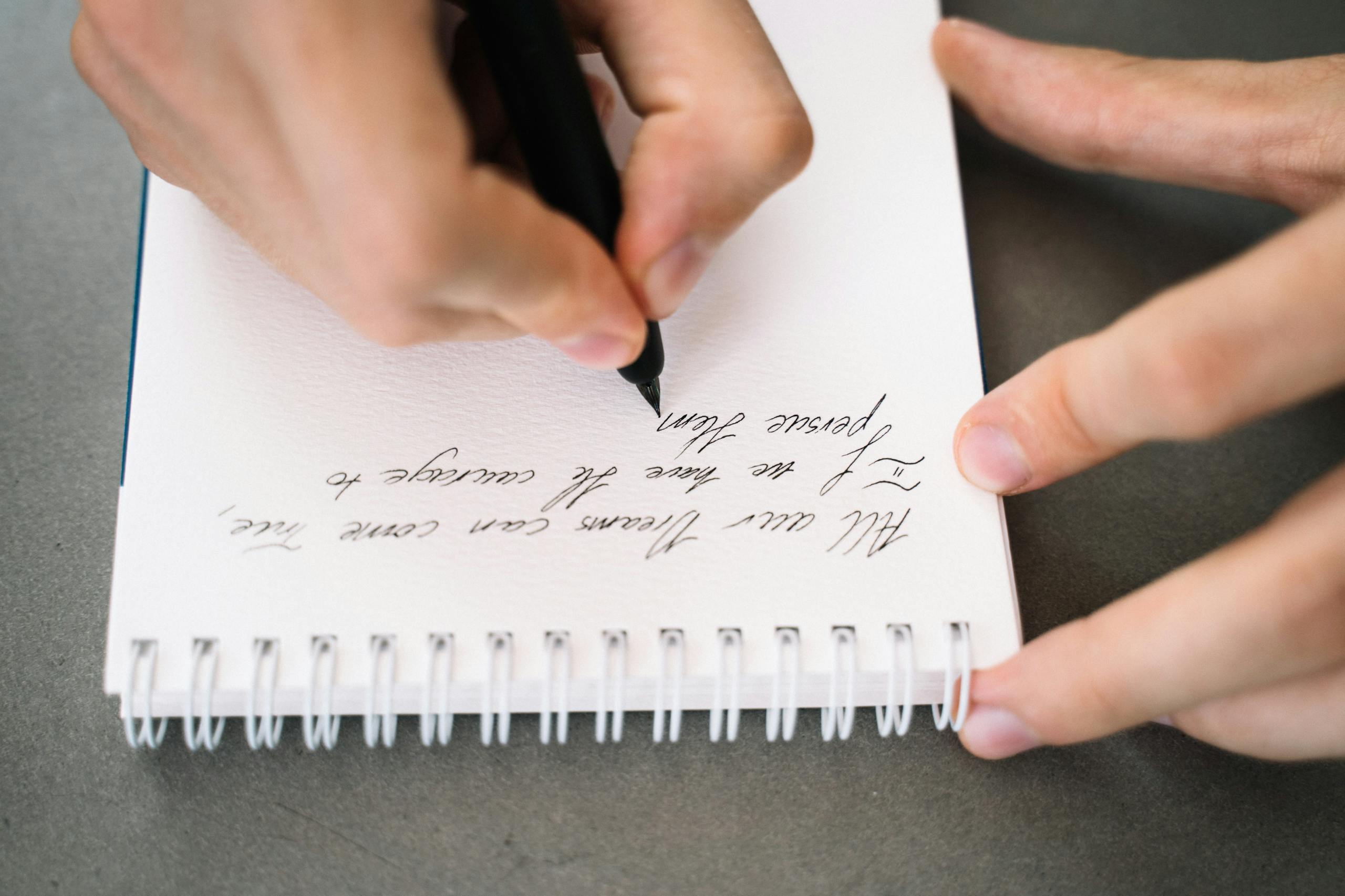 Hand holding a pen writing cursive in a notebook with elegant handwriting.
